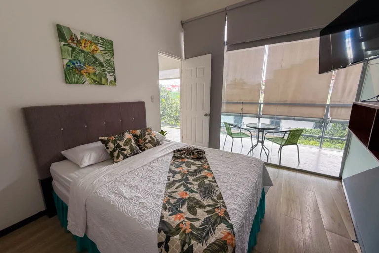 Bedroom with queen bed and private balcony overlooking greenery at Candó Living, San José